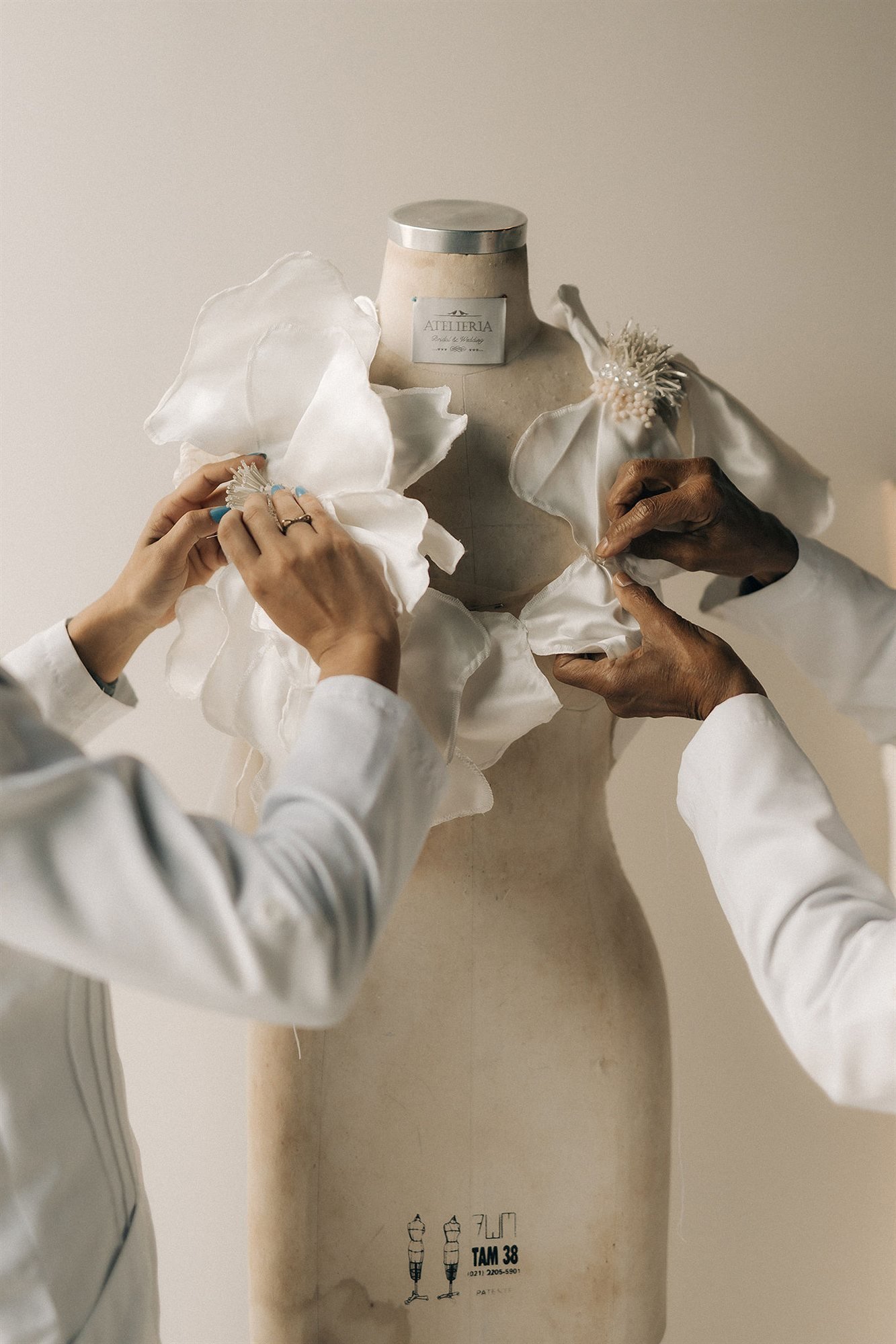 Mãos montando a peça em manequim de ateliê, a quatro mãos
